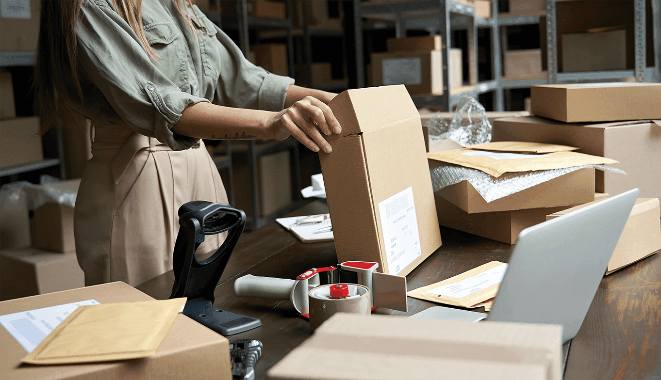 Mitarbeiter verpackt ein Paket mit Karton, Klebeband und Verpackungsmaterial am Arbeitstisch