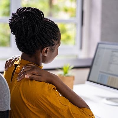 Büromitarbeiterin hält sich den Nacken als Beispiel für falsche Sitzhaltung am Arbeitsplatz